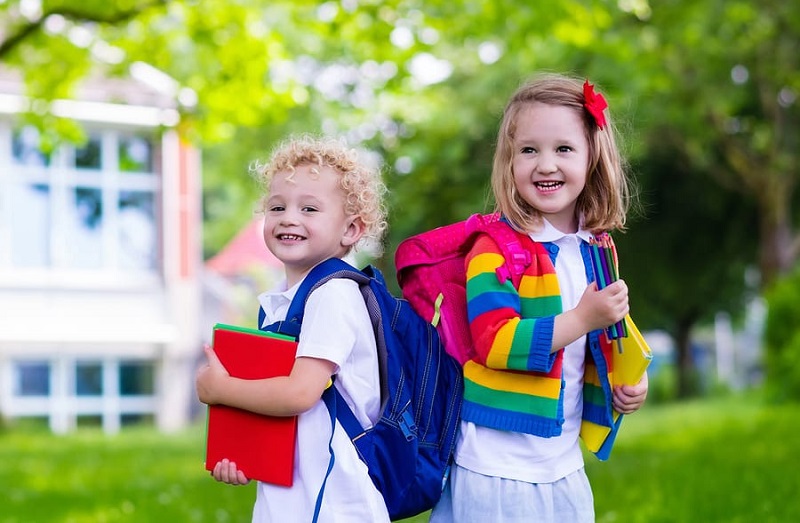 πρώτη δημοτικού παιδιά που γελάνε αγοράκι και κοριτσάκι με πολύχρωμες τσάντες στο δρόμο για το σχολείο